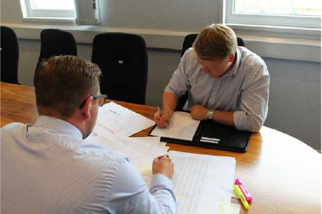Two male employees discussing a contract at a conference room table.